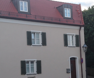 Cremefarbenes Haus mit dunkler Tür und Fensterläden und rotem Dach